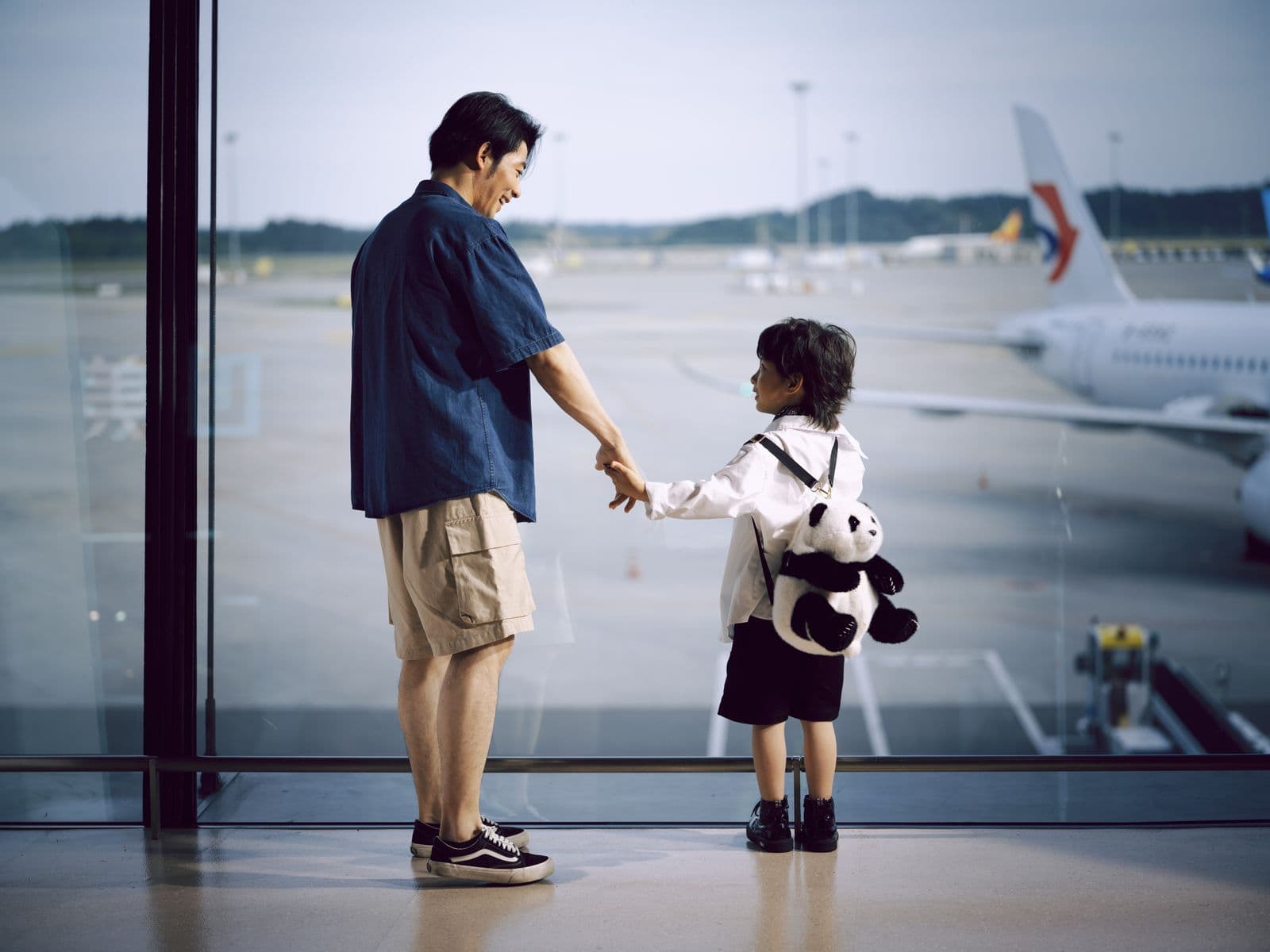 A parent and child watching aircraft through an airport window